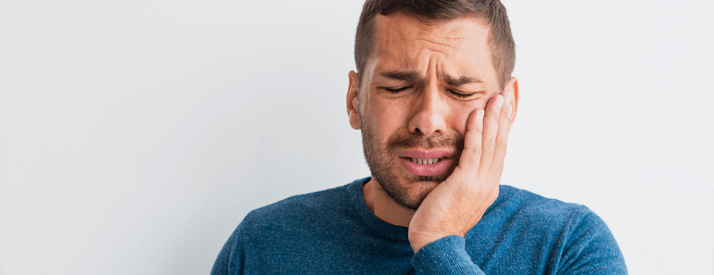 Man with Dental Discomfort - A photograph depicting a man holding his cheek in pain due to a dental issue